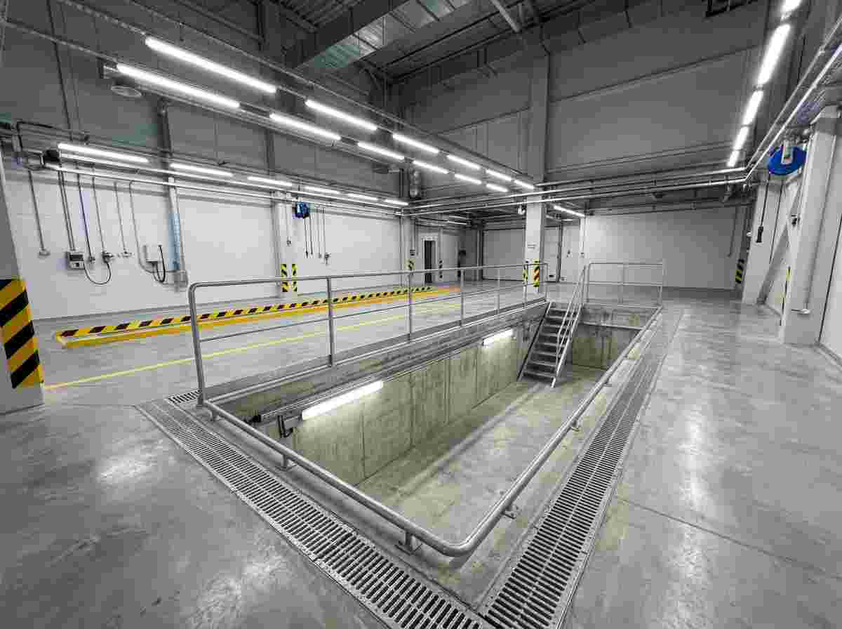 Leere Autowerkstatt mit rechteckiger Betontauchgrube, Geländer, Treppen, Sicherheitsbarrieren, Licht.