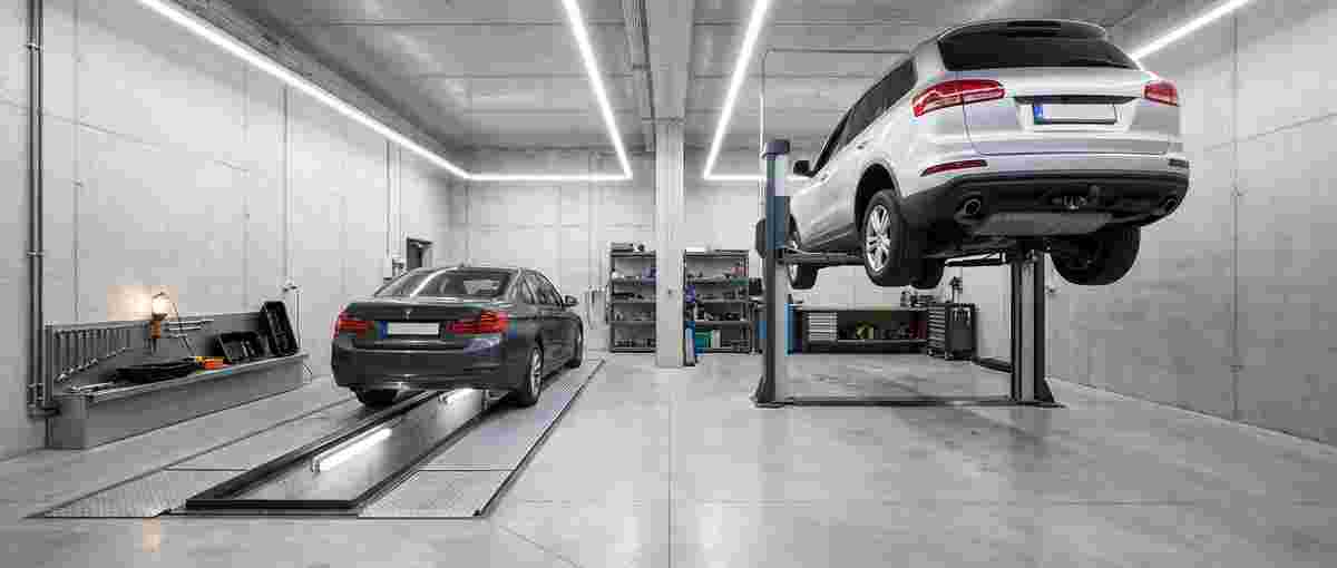 Grube oder Hebebühne von HDC: Zwei Autos sind zu sehen, eines auf Parkstreifen in einer Grube, ein anderes auf einer Hebebühne. Die Umgebung wirkt sehr sauber und modern mit hellen Neonröhren an der Decke.