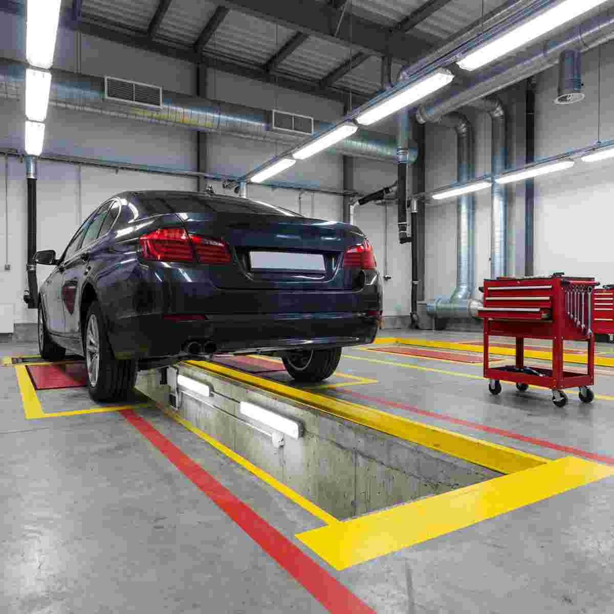 Fahrzeug-Grube in moderner Werkstatt; Auto darüber, Sicherheitszonen, Bodenlinien, Werkzeugwagen.