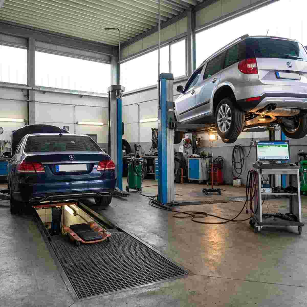Werkstatthalle mit einem Auto über einer Montagegrube und einem weiteren auf der Hebebühne