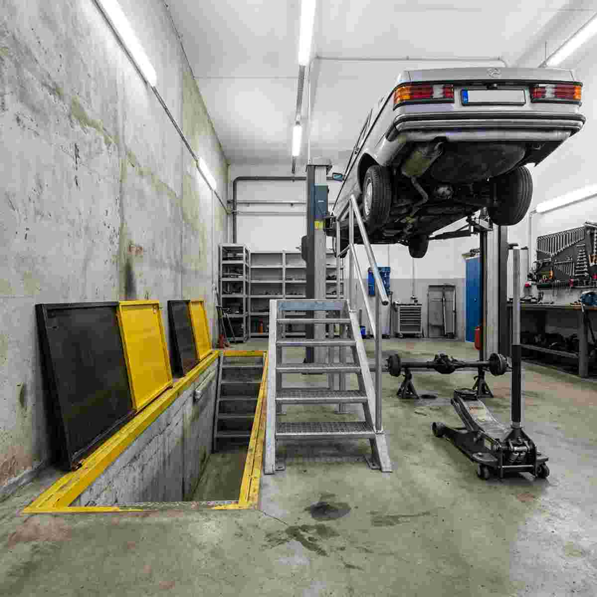 Werkstatt mit offener Grube, Auto darüber, Unterseite sichtbar, Grubenabdeckung, Treppen, Wagenheber