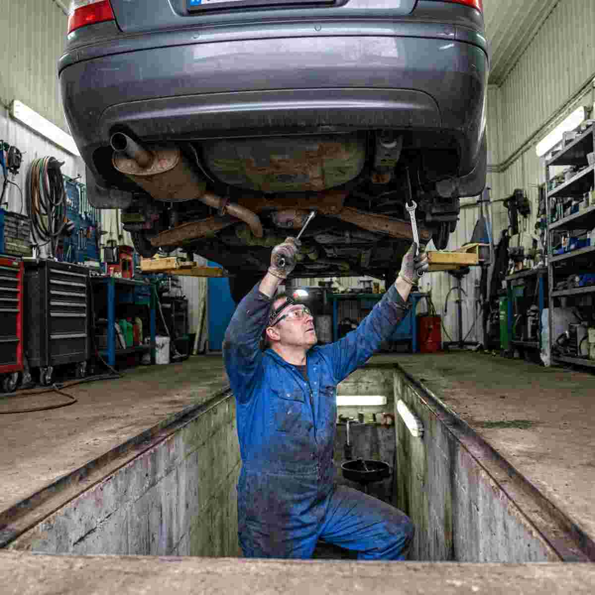 Mechaniker prüft unter einem Auto die Auspuffanlage und Bremskomponenten.