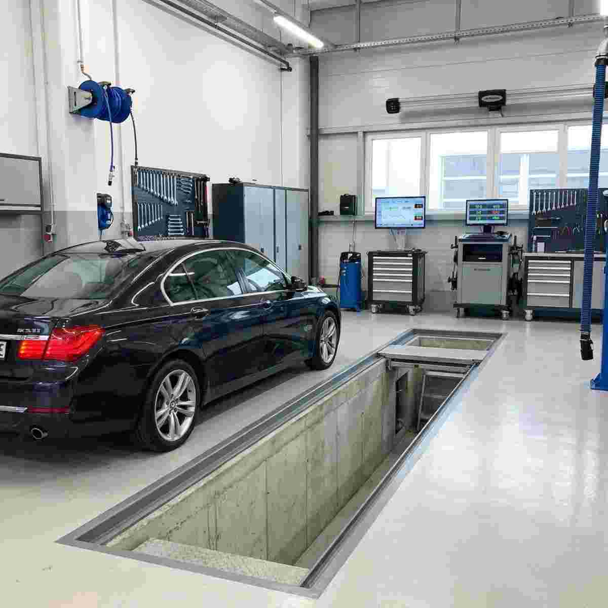 Fertig eingerichtete Werkstatthalle mit Auto über einer Arbeitsgrube und geordneten Geräten