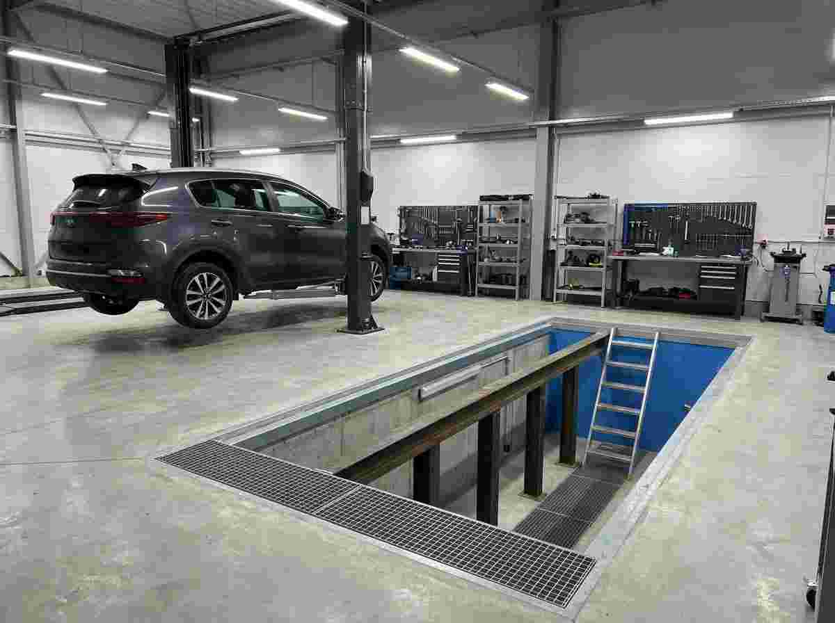 Hydraulischer Fahrzeuglift über offener Werkstattgrube, Fahrzeug oben, helle Arbeitsumgebung.