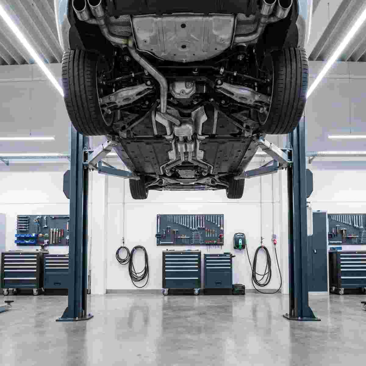 Quadratisches Bild moderner Autowerkstatt; Auto auf Hydrauliklift, Unterboden sichtbar.