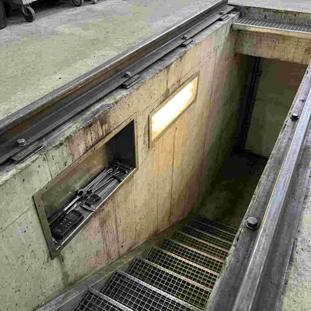 Innenansicht einer Montagegrube mit Führungsschienen, Werkzeugnische, Licht und Treppe